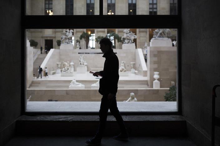 A man checks his phone as he walks past the Louvre museum in Paris, Saturday, Feb. 4, 2017. The Louvre in Paris reopened to the public Saturday morning, less than 24-hours after a machete-wielding assailant shouting "Allahu Akbar!" was shot by soldiers, in what officials described as a suspected terror attack. (AP Photo/Kamil Zihnioglu)
