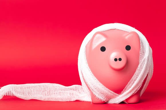 A piggy bank wrapped in bandages, against a red background.
