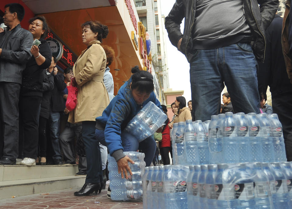 In this Friday, April 11, 2014 photo, a woman, center, tries to carry a pack of bottled water she bought as people line up to buy bottled water in the northwestern city of Lanzhou, Gansu province, China. An oil pipe leak caused excessive levels of the toxic chemical benzene in a major Chinese city's water supply, prompting warnings against drinking from the tap and sending residents to queue up to buy bottled water. (AP Photo) CHINA OUT