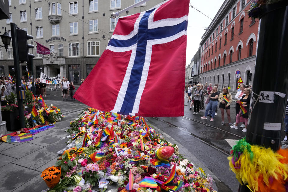 FILE - A Norwegian national flag flutters over flowers and rainbow flags that are placed at the scene of a shooting in central of Oslo, Norway, on June 26, 2022. The trial of a Norwegian citizen originally from Iran started Tuesday, March 12, 2024, in an Oslo court where he is accused of aggravated terrorism for a deadly shooting nearly two years ago ahead of an LGBTQ festival in the nightlife district of the Norwegian capital. Two people were killed and nine seriously wounded in the shooting at three locations, chiefly outside the London Pub, a popular gay bar, on June 25, 2022. (AP Photo/Sergei Grits)