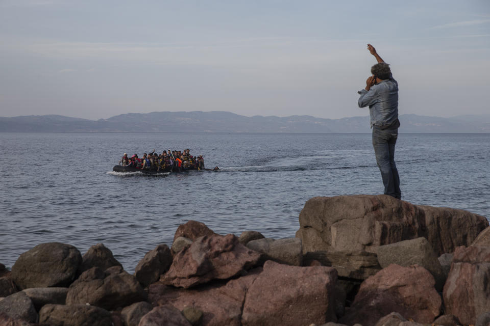 In this Wednesday, Sept. 9, 2015 photo refugees and migrants aboard an overcrowded dinghy as they cross the Aegean Sea, from Turkey, that is seen in the background, to the coast of Lesbos island, Greece. Greek authorities have invited private contractors to bid on supplying a 2.7-kilometer-long (1.7 miles) floating barrier system aimed at stopping migrants from reaching the country's islands from the nearby coast of Turkey. (AP Photo/Petros Giannakouris)