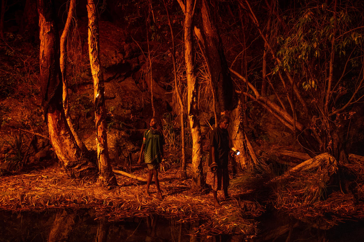 This image provided by World Press Photo which won the World Press Photo Story Of The Year award by Matthew Abbott for National Geographic Magazine/Panos Pictures, titled Saving Forests With Fire, shows Stacey Lee, 11-years-old, left, setting the bark of trees alight to produce a natural light source to help hunt for file snakes (Acrochordus arafurae), in Djulkar, Arnhem Land, Australia, on 22 July 2021. (Matthew Abbott for National Geographic/Panos Pictures/World Press Photo via AP)