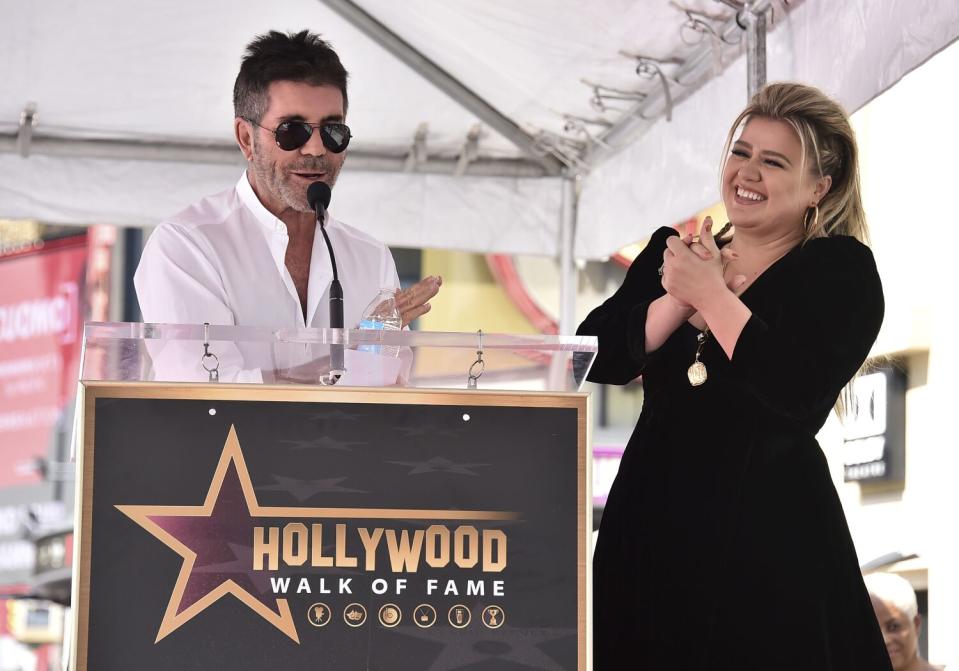 A man in sunglasses speaks at a lectern while a smiling woman looks on.