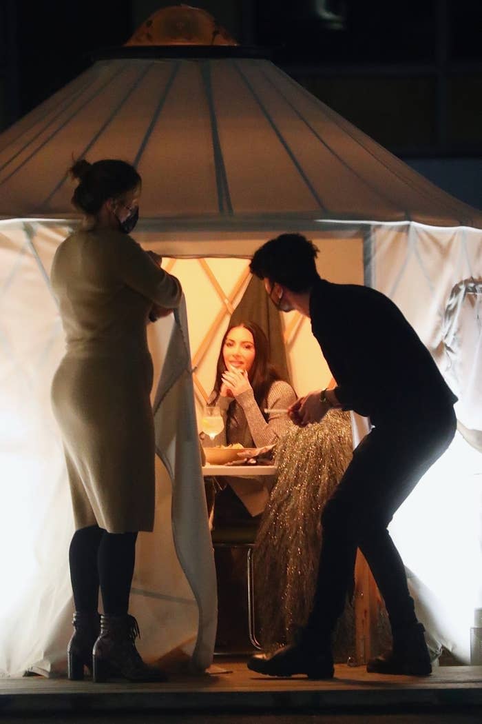 Kim sitting in a yurt at a restaurant as a waiter looks in and another person holds the entrance flap open