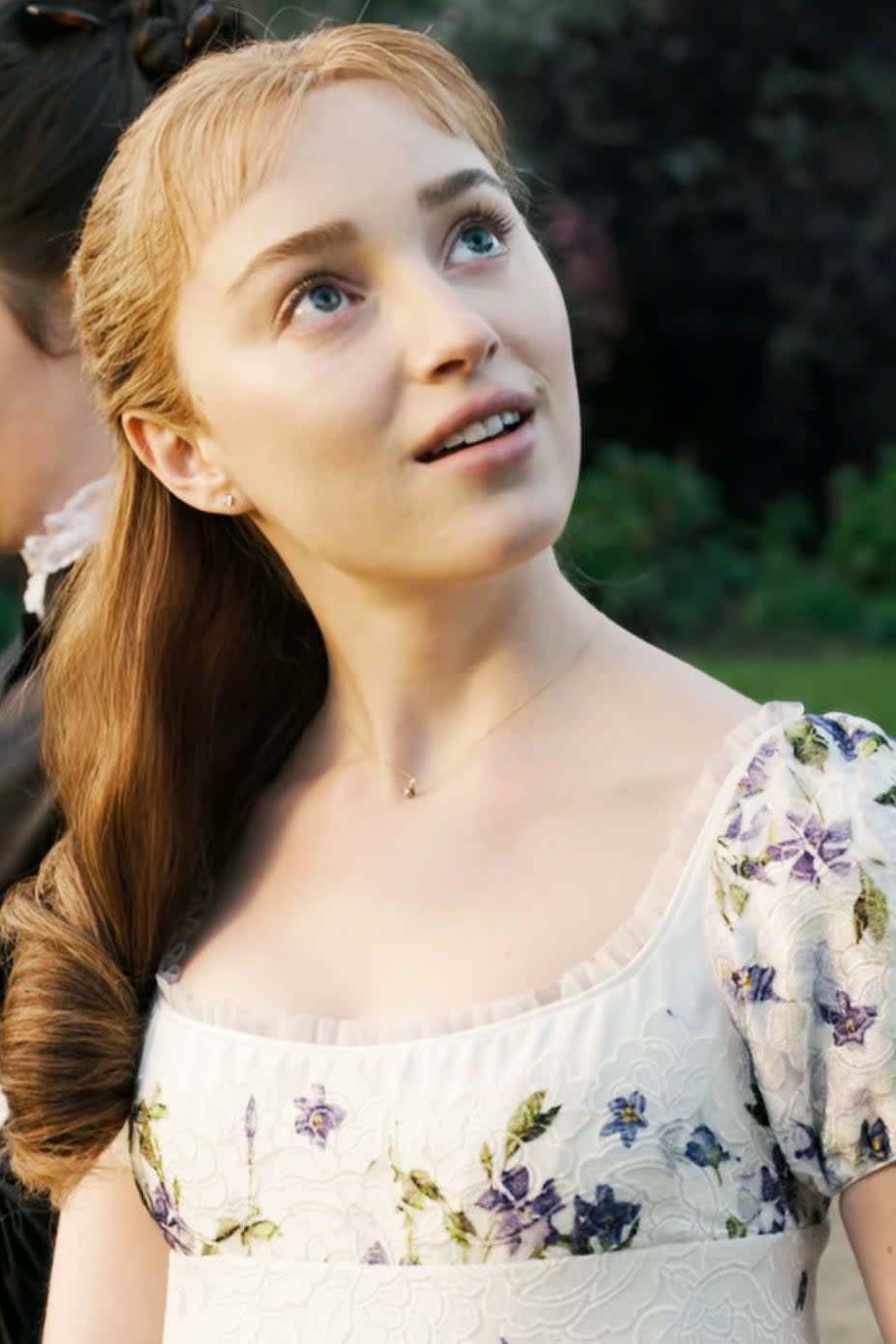 Phoebe Dynevor as Daphne looking upwards at someone else with a serene expression as they walk