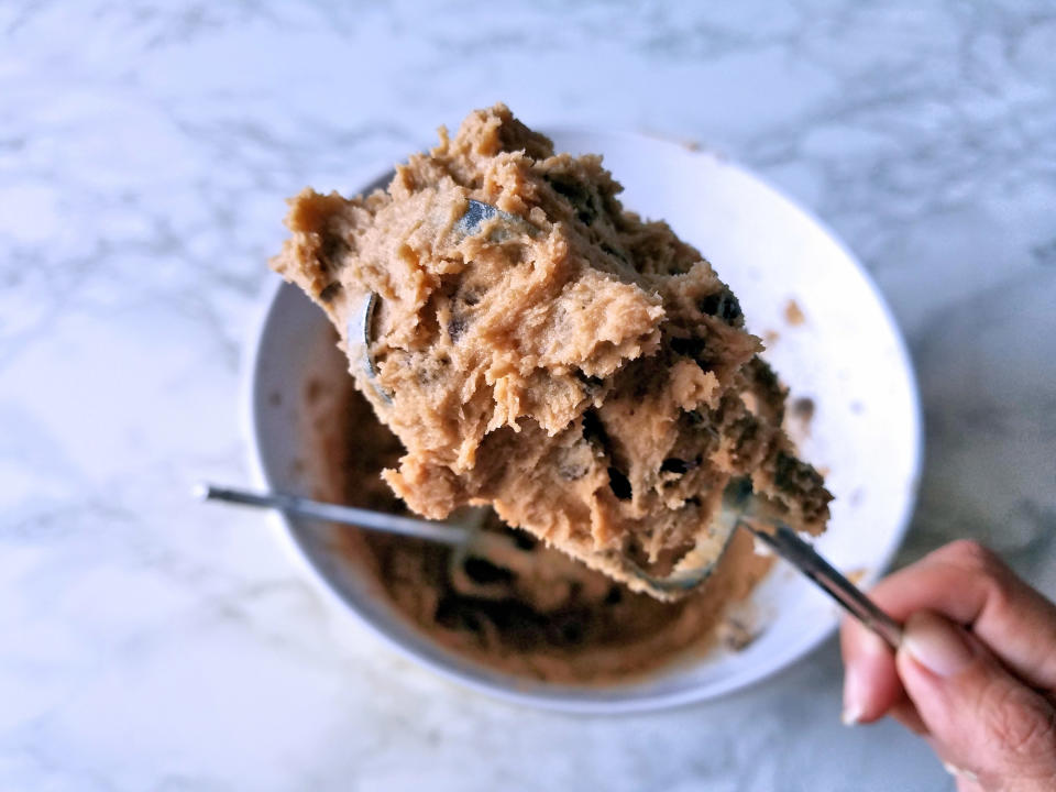 Raw cookie dough on a mixer above a bowl of cookie dough.