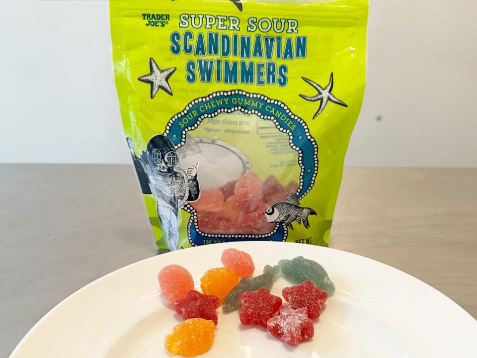 Green bag of Trader Joe's super-sour Scandinavian swimmers with red, green, and orange candies on a plate in foreground