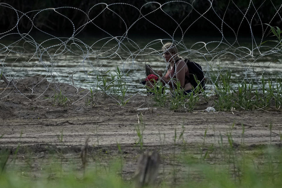 Migrantes caminan entre alambre de púas mientras tratan de cruzar el río Bravo en la frontera de Estados Unidos con México, en Eagle Pass, Texas, el jueves 6 de julio de 2023. (AP Foto/Eric Gay)