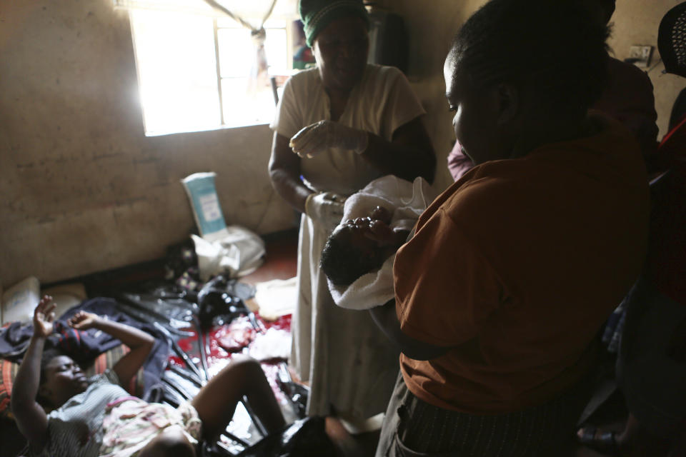 A woman holds a baby delivered in a tiny apartment in the poor suburb of Mbare in Harare, Zimbabwe, Saturday, Nov. 16, 2019, after the baby was delivered with the help of 72-year old grandmother Esther Zinyoro Gwena. Grandmother Esther Zinyoro Gwena claims to be guided by the holy spirit and has become a local hero, as the country’s economic crisis forces closure of medical facilities, and mothers-to-be seek out untrained birth attendants.(AP Photo/Tsvangirayi Mukwazhi)