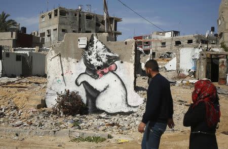 Palestinians walk past a mural of a playful-looking kitten, presumably painted by British street artist Banksy, on the remains of a house that witnesses said was destroyed by Israeli shelling during a 50-day war last summer, in Biet Hanoun town in the northern Gaza Strip February 26, 2015. REUTERS/Suhaib Salem