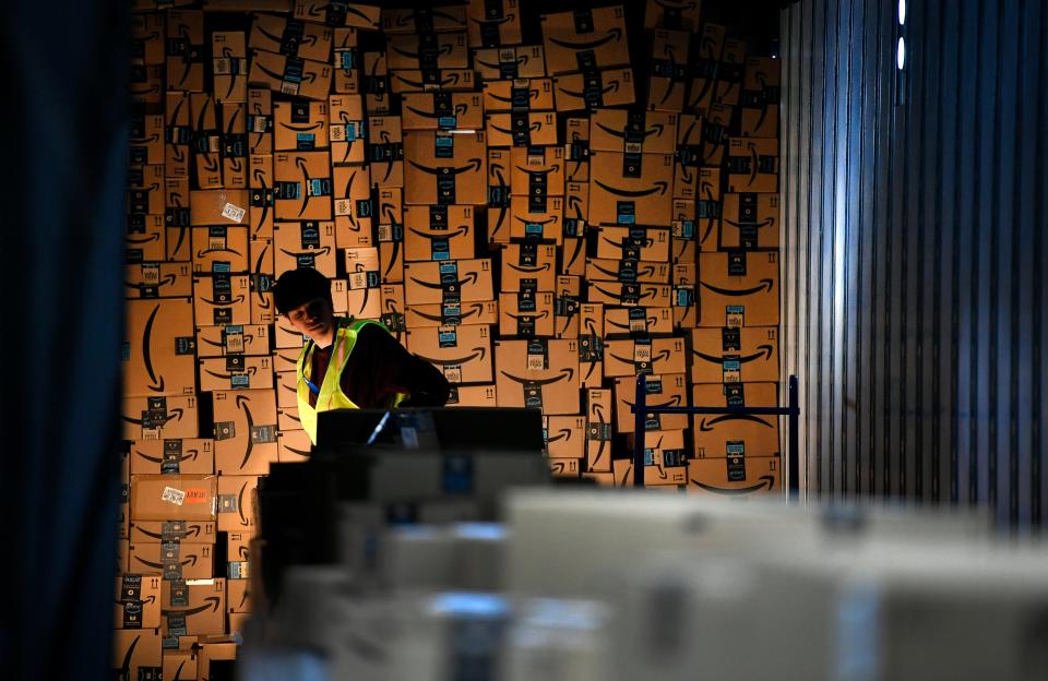 A young man is illuminated in an otherwise dark space surrounded by stacks of Amazon cardboard boxes.