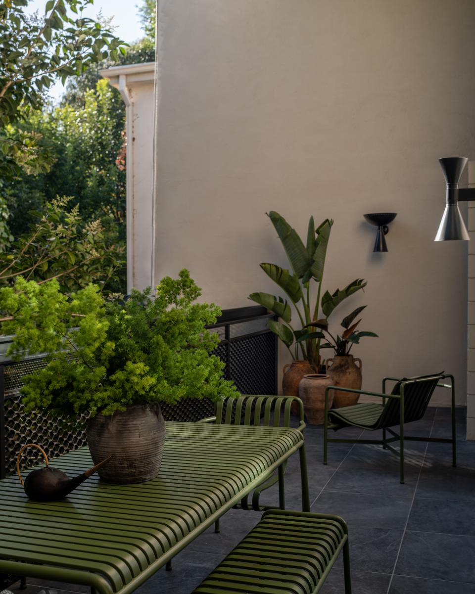 The terrace flows in from the landscape, giving the home an Eden-like ending. The seating, which includes a Palissade exterior dining set and armchair by Hay, is disguised amidst the greenery. A metallic Le Corbusier Applique de Marseille wall sconce and a restored black wall lamp halo the setting come sundown.