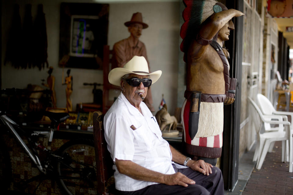 FILE - This April 30, 2014 photo shows Pedro Bello sits outside his Cuba Tobacco Cigar Factory on Calle Ocho (Eighth Street) in Miami's Little Havana. Once a refuge for Cuban exiles rekindling the tastes and sounds a lost home, today Miami’s Little Havana is a mosaic of cultures and a popular tourist destination. (AP Photo/J Pat Carter)