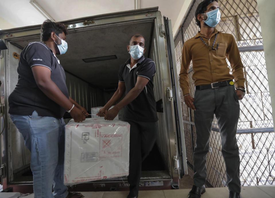 A Sri Lankan health services workers unload a consignment of Oxford-AstraZeneca vaccine donated by the Indian government at a medical warehouse as a plain clothed police officer stands guard in Colombo, Sri Lanka, Thursday, Jan. 28, 2021. Sri Lanka's president on Thursday welcomed the first 500,000 doses of a COVID-19 vaccine from India, which has donated the shots to eight countries in the region. (AP Photo/Eranga Jayawardena)