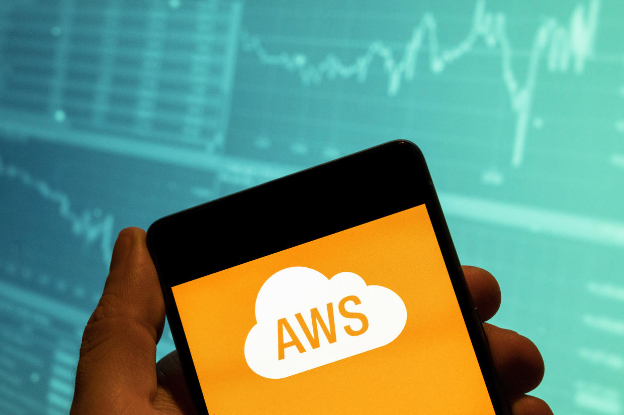 CHINA - 2023/03/16: In this photo illustration, the American on-demand cloud computing platform owned by Amazon, Amazon Web Services AWS logo is seen displayed on a smartphone with an economic stock exchange index graph in the background. (Photo Illustration by Budrul Chukrut/SOPA Images/LightRocket via Getty Images)