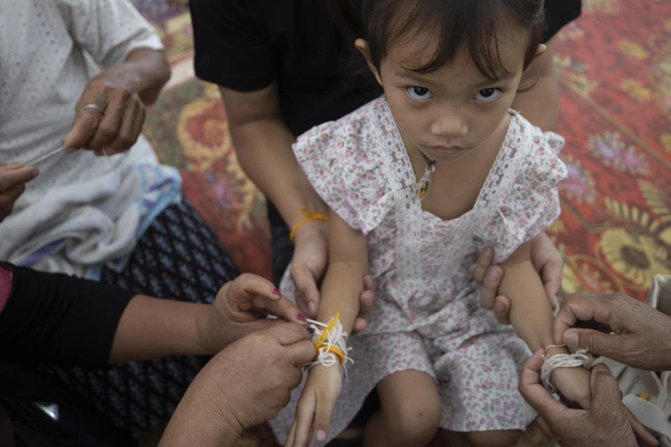Relatives of the victims of the mass killing attack tie holy threads on the wrists of 3 year old Paweenuch Supolwong, the only child to emerge unscathed, inside Wat Rat Samakee temple in Uthai Sawan, north eastern Thailand, Saturday, Oct. 8, 2022. A former police officer burst into a day care center in northeastern Thailand on Thursday, killing dozens of preschoolers and teachers before shooting more people as he fled. (AP Photo/Wason Wanichakorn)