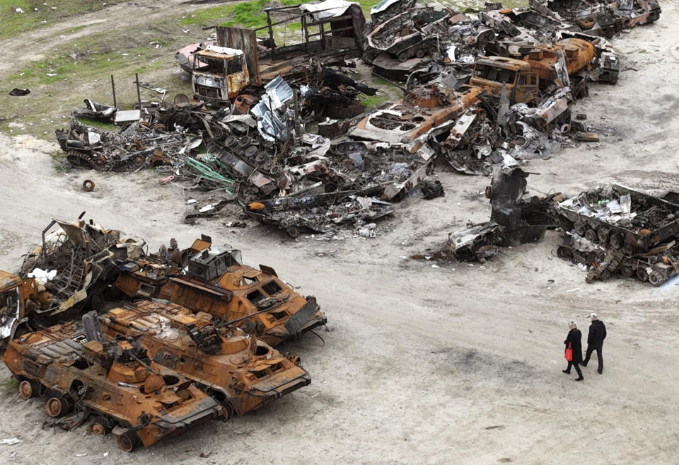 People walk past wrecks of military vehicles in Bucha, on the outskirts of Kyiv, Ukraine, Saturday, April 30, 2022. (AP Photo/Emilio Morenatti)