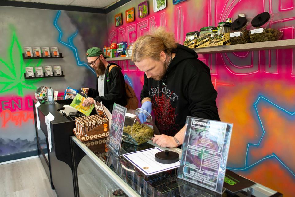 Casey Marler selects a product for a customer while Aaron Crooke, left, checks in new products at the Green Light District on Tuesday.