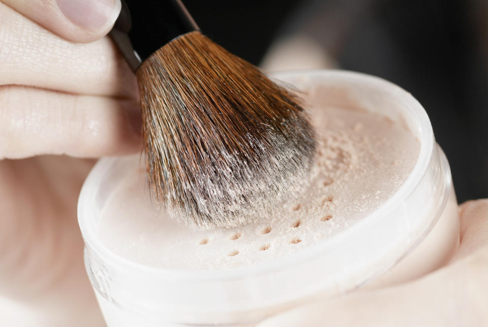 Close up of loose powder and hand holding makeup brush