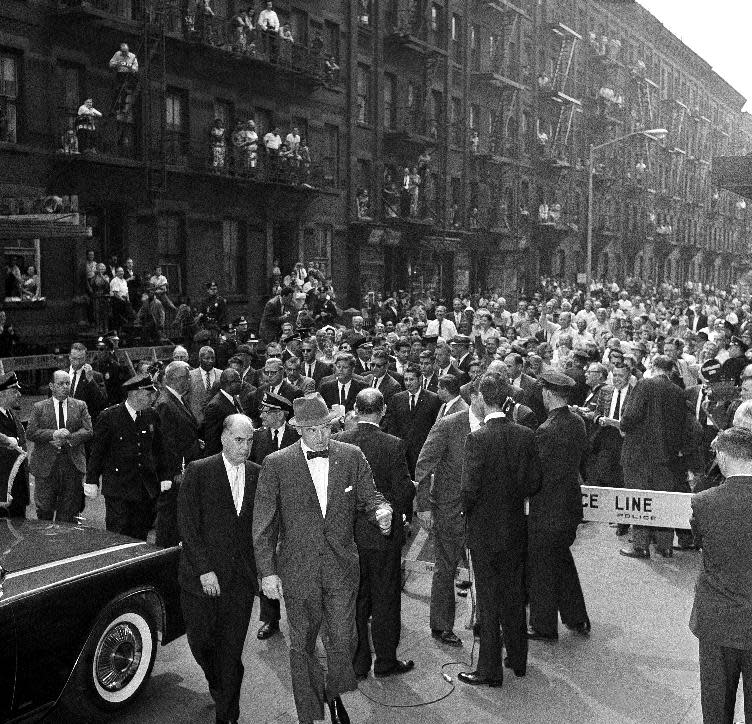 FILE - In this May 20, 1962, file photo Midtown Manhattan residents line the fire escapes to watch President John F. Kennedy, at center above man with hat in foreground, walk along West 49th Street in New York under a cordon of police and Secret Servicemen, as he make his way to Madison Square Garden to address a rally in support of his administration’s Medicare program for the elderly. Though he made health care a major campaign issue, as president he can't get a plan for the elderly through Congress. (AP Photo/File)