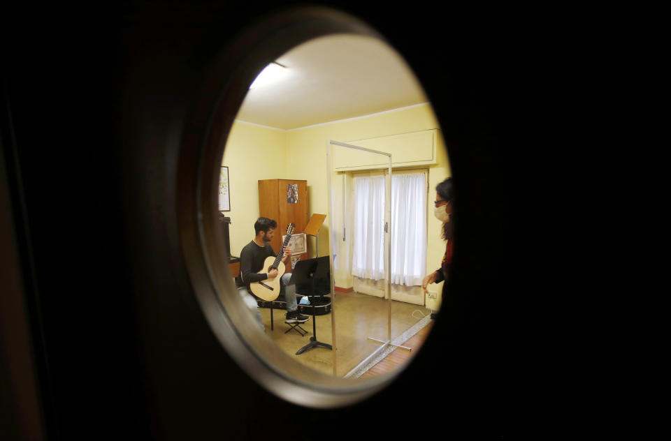 Carlo D'Ariano is seen through a window as he plays his guitar behind a transparent panel to curb the spread of COVID-19, during a lesson with maestro Maria Vittoria Jedlowski at the Giuseppe Verdi Music Conservatory, in Milan, Italy, Thursday, April 29, 2021. Whatever the instrument, flute, violin or drums, students at Italy's oldest and largest music conservatory have been playing behind plexiglass screens during much of the pandemic as the Conservatory found ways to preserve instruction throughout Italy’s many rolling lockdowns. (AP Photo/Antonio Calanni)