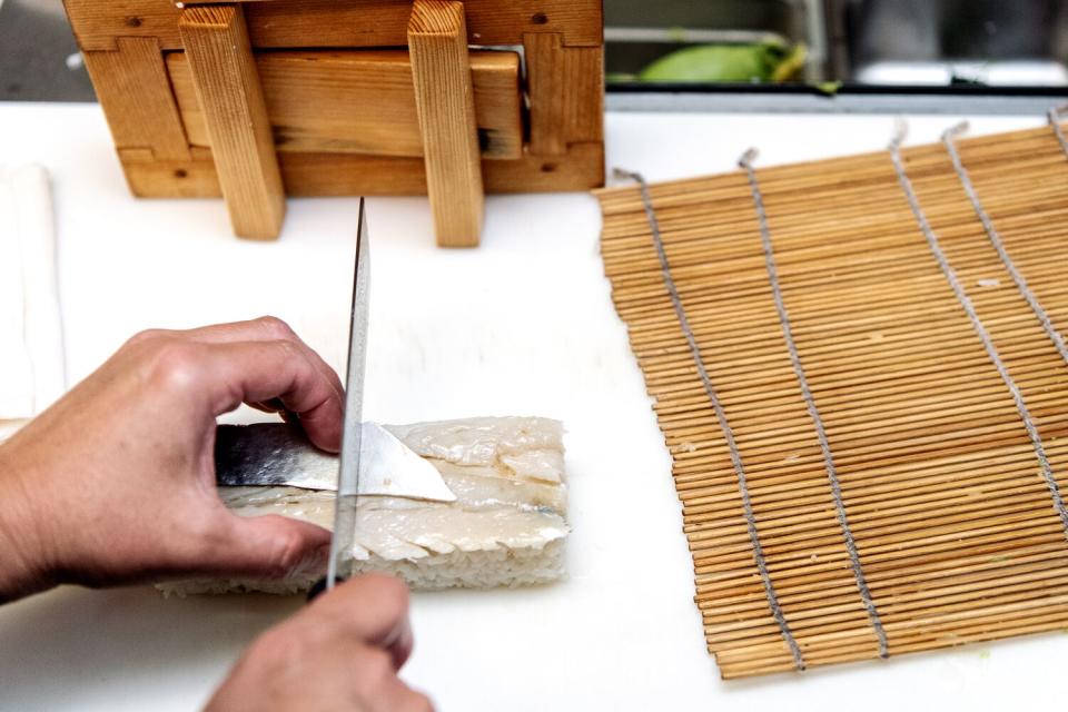 Hands hold a knife cutting a block of sushi.