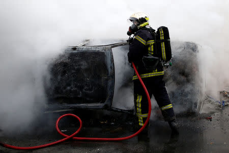 A French fireman extinguishes a burning car as youths and high school students protest against the French government's reform plan, in Nantes, France, December 6, 2018. REUTERS/Stephane Mahe