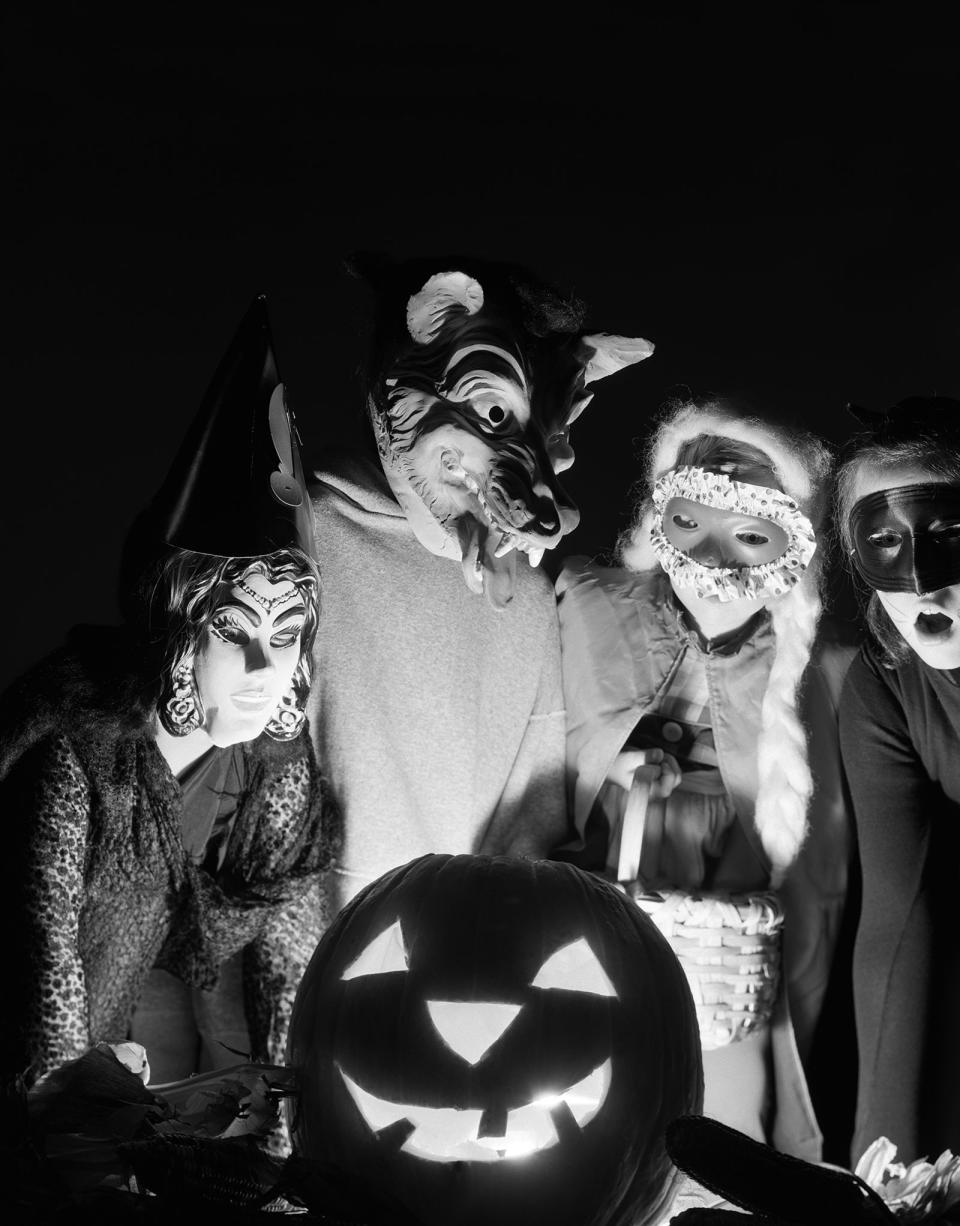 <p>Four masked trick-or-treaters gather around a jack-'o-lantern in the 1960s. </p>