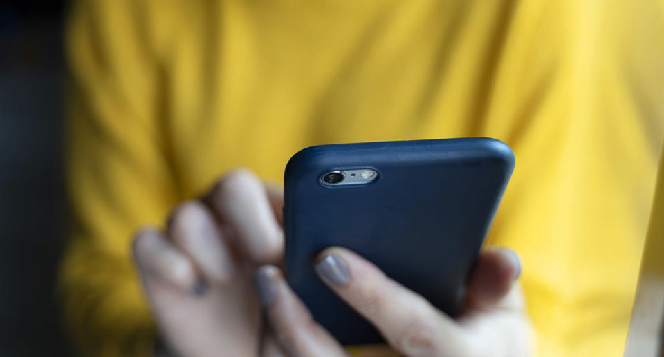 Woman in a yellow pullover, using smartphone.