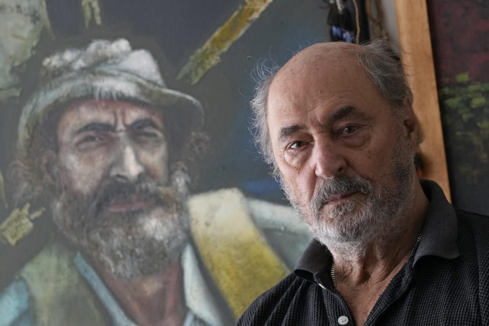 Veteran ethnographer Sydney Possuelo poses for a photo next to a painting made in his honor for the work he carried out in the demarcation of Indigenous territories, in his apartment in Brasilia, Brazil, Monday, May 30, 2022. Possuelo, who once headed the nation's Indigenous agency, was shocked when he heard Brazil's President Jair Bolsonaro received the Medal of Indigenous Merit. He protested by returning his own medal, which he received 35 years prior. (AP Photo/Eraldo Peres)