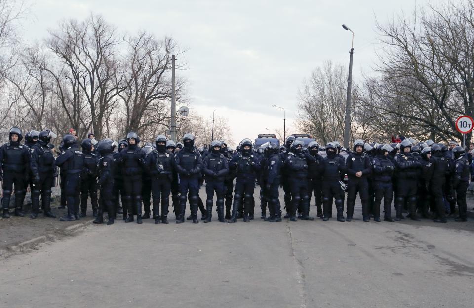 Ukrainian riot police gather to block protesters who planned to stop buses carrying passengers evacuated from the Chinese city of Wuhan, speak to Ukrainian riot police blocking the road outside Novi Sarzhany, Ukraine, Thursday, Feb. 20, 2020. Several hundred residents in Ukraine's Poltava region protested to stop officials from quarantining the evacuees in their village because they feared becoming infected. Demonstrators put up road blocks and burned tires, while Ukrainian media reported that there were clashes with police, and more than 10 people were detained. (AP Photo/Efrem Lukatsky)