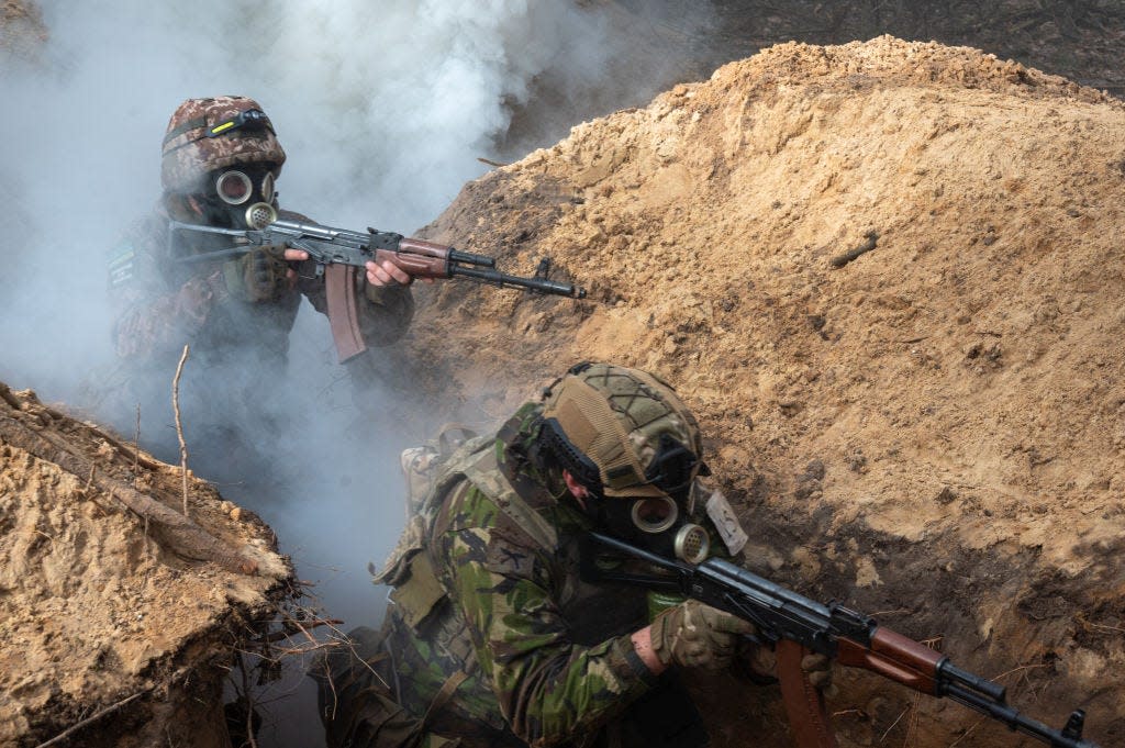 Two soldiers in trenches wearing gas masks and carrying guns.