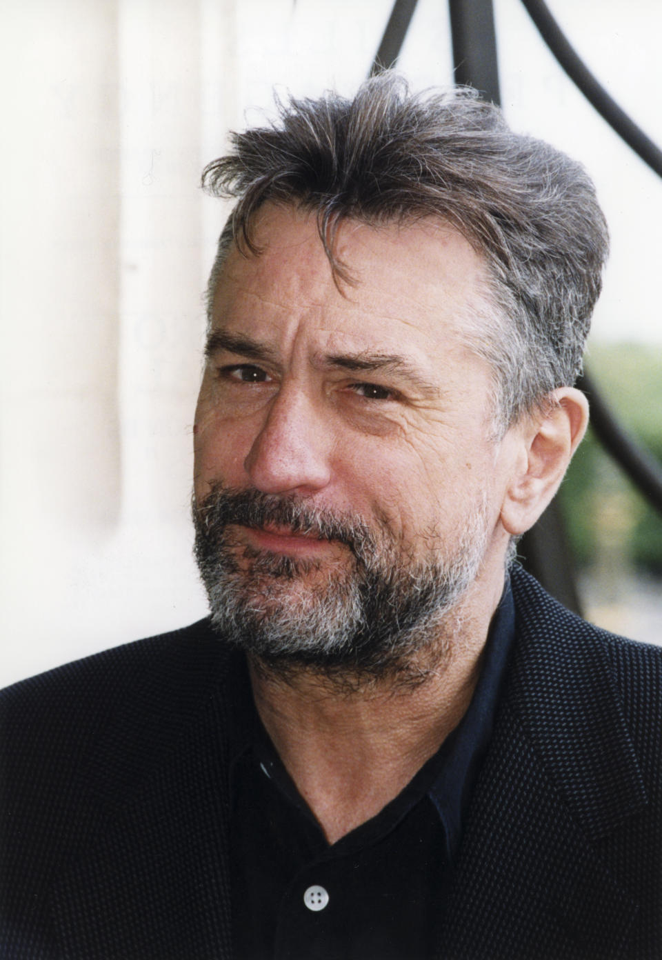 Close-up of a man with a beard and mustache, wearing a collared shirt and blazer