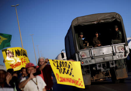 A truck carrying army officials passes by people supporting the truck owners striking in protest against high diesel prices in Luziania, Brazil May 27, 2018. The sign reads "We are all truckers". REUTERS/Ueslei Marcelino