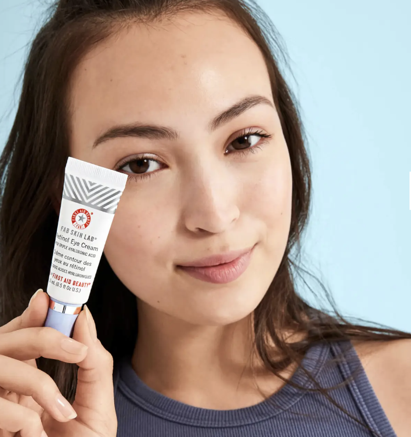 A young lady holds on to First Aid Beauty Skin Lab Retinol Eye Cream with Triple Hyaluronic Acid near her face