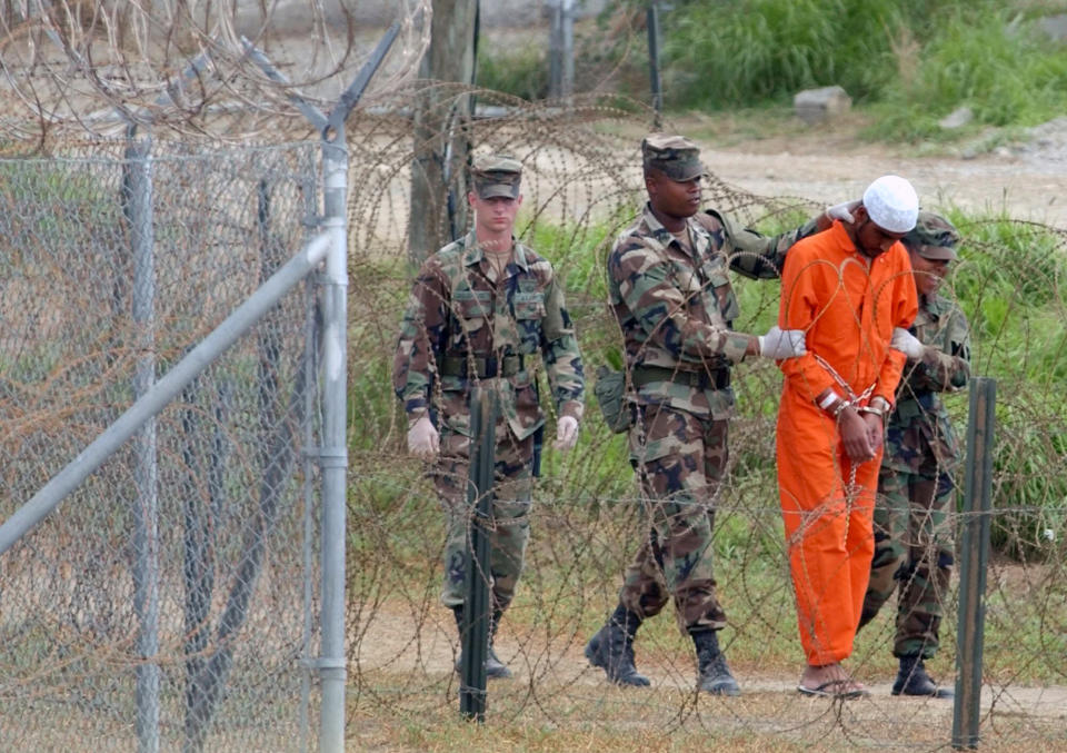 FILE - In this Feb. 6, 2002, file photo a detainee is led by military police to be interrogated by military officials at Camp X-Ray at the U.S. Naval Base at Guantanamo Bay, Cuba. At the time the image was taken there were 158 al-Qaida and Taliban prisoners being held at Camp X-Ray. The 20th anniversary of the first prisoners' arrival at the Guantanamo Bay detention center is on Tuesday, Jan. 11, 2022. There are now 39 prisoners left. At its peak, in 2003, the detention center held nearly 680 prisoners. (AP Photo/Lynne Sladky, File)