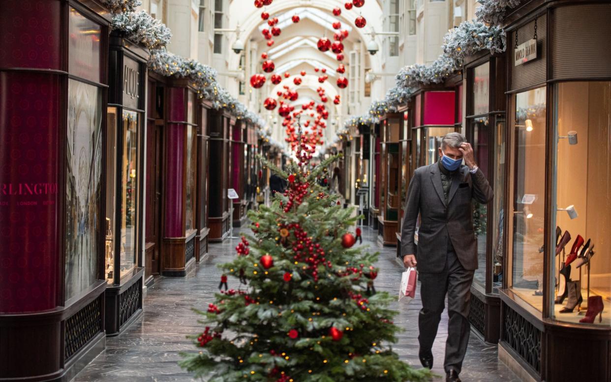 A man wearing a face mask passes Christmas decorations in the Burlington Arcade, London, as England continues a four week national lockdown to curb the spread of coronavirus - Dominic Lipinski/PA