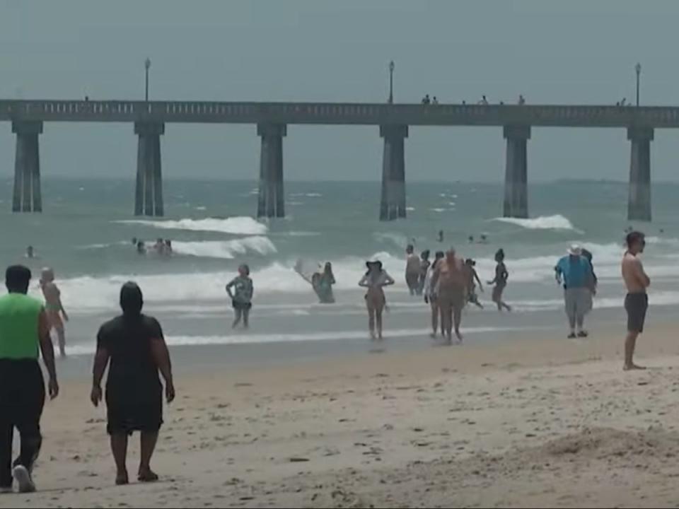 Beachgoers mill around the beach and play in the surf at Carolina Beach, North Carolina. More than 90 people had to be rescued from rip currents during the second-to-last weekend of June 2024 at the beach (screengrab/CBS17)