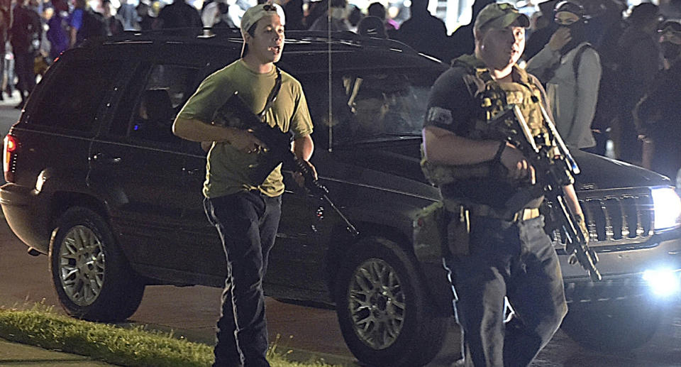 Kyle Rittenhouse, left, with backwards cap, walks along in Kenosha holding a rifle. 