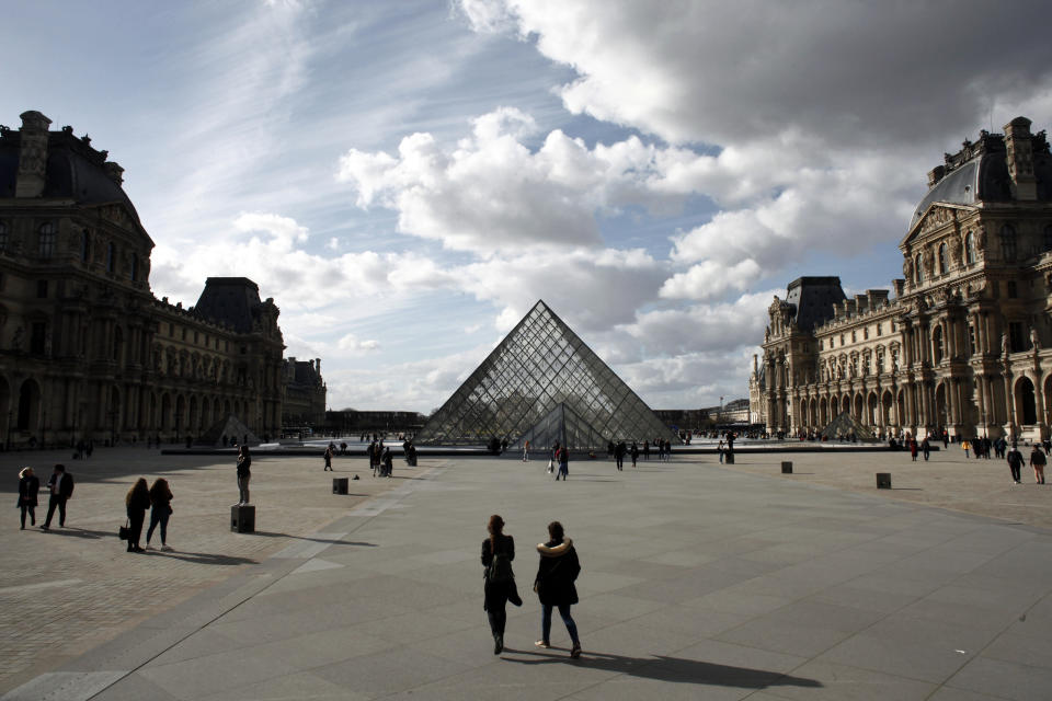 FILE - In this March 13, 2020 file photo, people walk by the Louvre Museum, in Paris. Iconic sites that are among some of France's biggest tourist draws won't reopen when the country lifts most of its coronavirus restrictions next week. Neither the Louvre Museum, the Eiffel Tower nor the Versailles Palace will be reopening next week when France lifts many of its remaining coronavirus lockdown restrictions. (AP Photo/Thibault Camus, File)