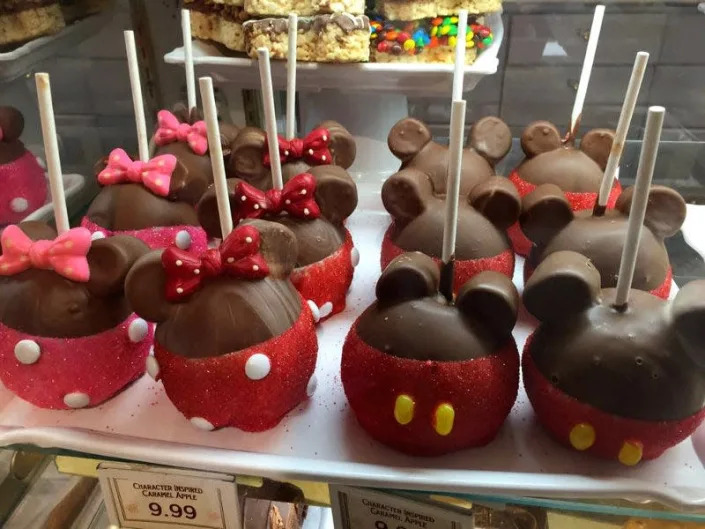 Chocolate covered apples with sticks and Minnie and Mickey mouse ears, bows, and clothing designs.