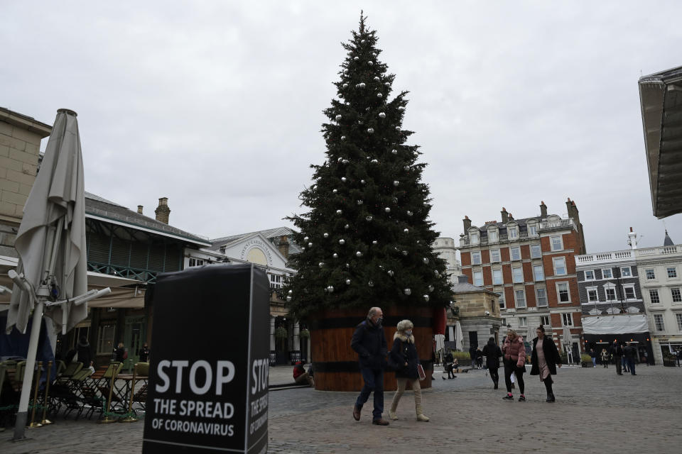 People wearing face masks walk past a Christmas tree in Covent Garden, during England's second coronavirus lockdown in London, Thursday, Nov. 26, 2020. Most people in England will continue to face tight restrictions on socializing and business after a nationwide lockdown ends next week, the government announced Thursday. (AP Photo/Matt Dunham)