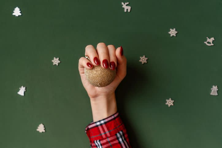 christmas manicure red nails hands in checkered shirt hold golden ball on green background with silver baubles