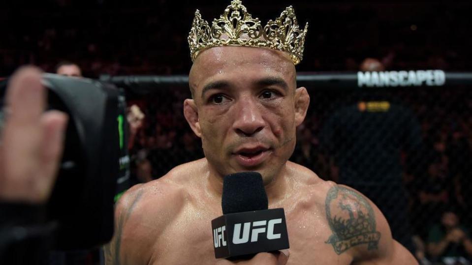Jose Aldo wears a crown as he speaks on a UFC microphone after a fight