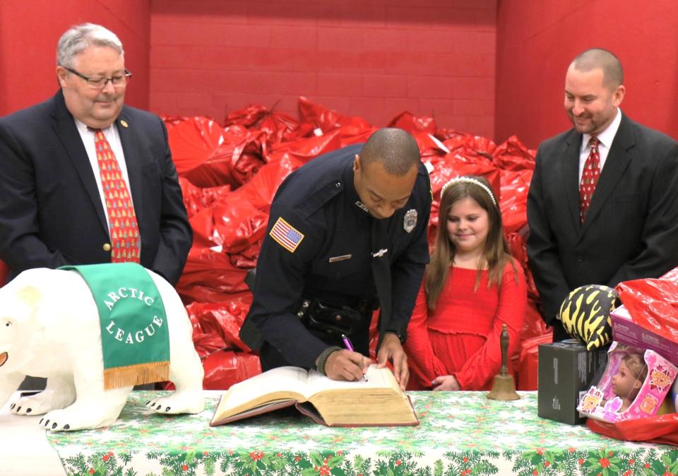 Elmira police officer Bryant Tranchant signs the Arctic League Big Book on Friday, Dec. 15, 2023, after making a $2,500 donation on behalf of the Elmira Police Benevolent Association. Looking on are Arctic League Treasurer Mike Wayne, left, bell ringer Annie McKenzie and board President Scott Heffner.