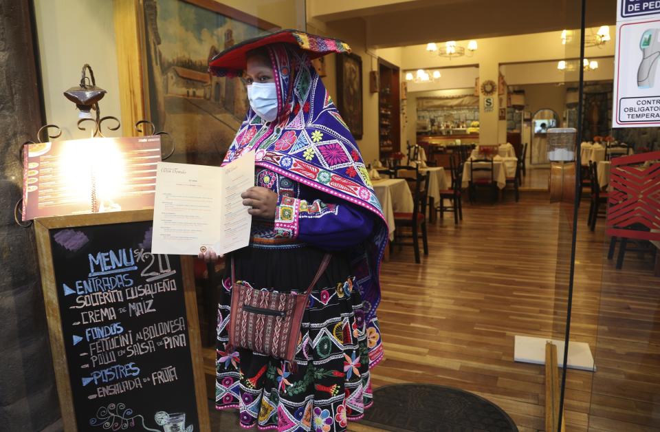 Una camarera vestida con ropa tradicional muestra el menú de un restaurante vacío en medio de la pandemia de COVID-19 en Cusco, Perú, el viernes 30 de octubre de 2020. La pandemia ha provocado que Cusco, la capital de los Incas y que vive casi por completo del turismo internacional, se encuentre sumida en la peor crisis de su historia reciente. (Foto AP/Martín Mejía)