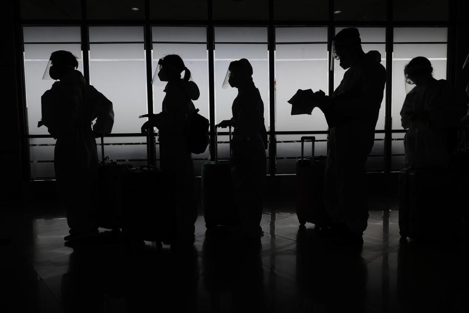 Foreign passengers wearing protective suits prepare for their flight to China at Manila's International Airport, Philippines, Monday, Jan. 18, 2021. Coronavirus infections in the Philippines have surged past 500,000 in a new bleak milestone with the government facing criticisms for failing to immediately launch a vaccination program amid a global scramble for COVID-19 vaccines. (AP Photo/Aaron Favila)