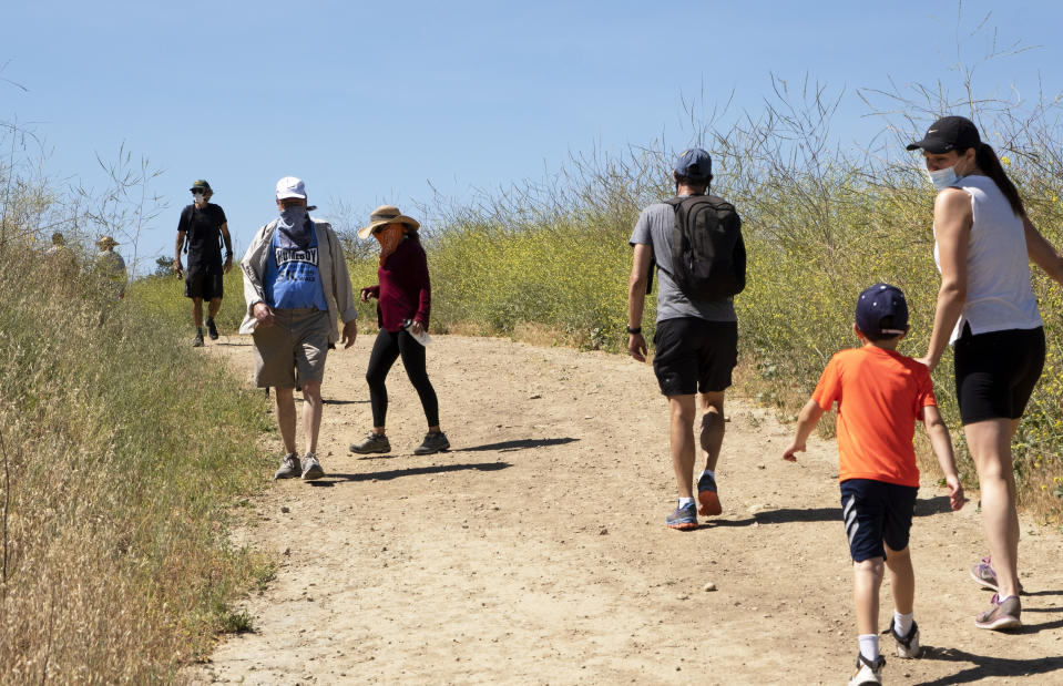 Visitors wear protective masks and social distance on a walk along a popular hiking trail along the Santa Monica mountain range in the Encino section of Los Angeles, Saturday, May 16, 2020. Leaving home in Los Angeles now requires bringing a face covering, part of the price for reopening more businesses and activities in America's second-largest city, which is moving cautiously as less-populated areas of California press ahead. (AP Photo/Richard Vogel)