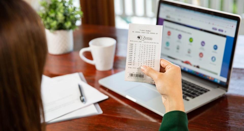 Woman holding up Oz Lotto ticket in front of laptop computer