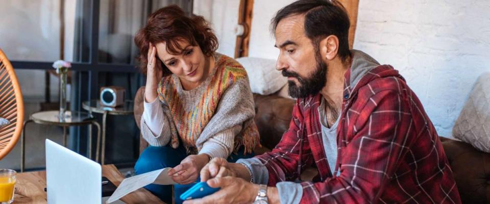 Couple sitting on the couch at home, looking at their financial statements, stressed.